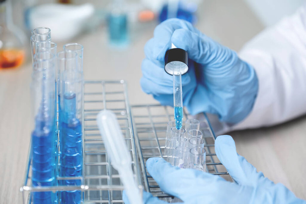Los científicos sostienen la pipeta y dejan caer el líquido químico azul para su investigación y análisis en un laboratorio. - Foto, Imagen