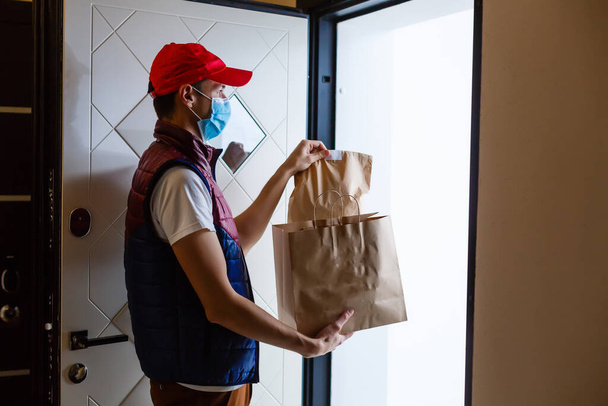 Uomo di consegna con sacchetto di carta con cibo su sfondo bianco, uomo di consegna del cibo in maschera protettiva - Foto, immagini