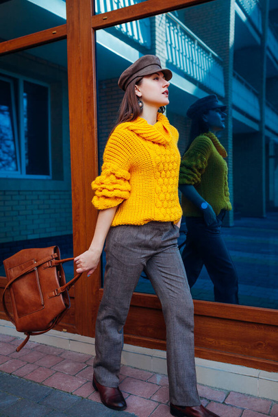 Stylish woman wears oversize yellow sweater, cap, trousers. holds stylish handbag. Autumn female clothes and accessories. Fashion - Fotoğraf, Görsel