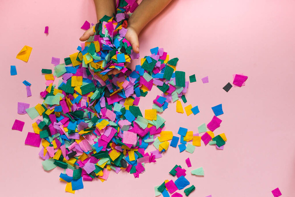 childrens hands throwing colorful confetti. top view on a pink background - Foto, Imagen