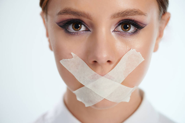 Scared young woman portrait eith tears and taped mouth close up view - Photo, Image