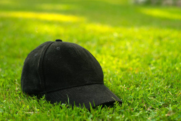Casquette textile noire sur herbe verte, fond flou, espace pour le texte - Photo, image