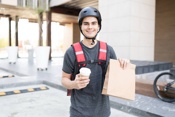 Selbstbewusster hispanischer Zusteller mit Paket und Einweg-Kaffeetasse - Foto, Bild