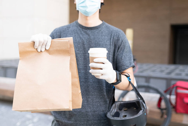 Midsection del repartidor con paquete y taza de café desechable durante la pandemia - Foto, imagen