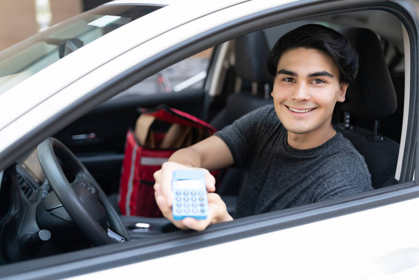Uśmiechnięty młody dostawca pokazujący czytnik kart kredytowych z samochodu - Zdjęcie, obraz