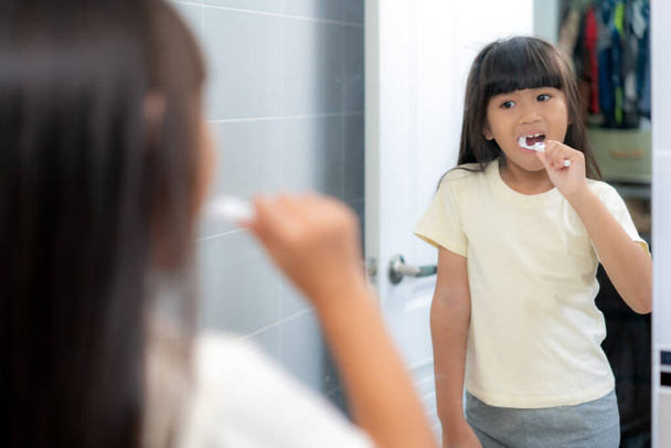 Cute Asian uczennica mycie zębów i patrząc w lustrze w łazience w domu. Rano szkolna rutyna w życiu szykuje się do szkoły. - Zdjęcie, obraz