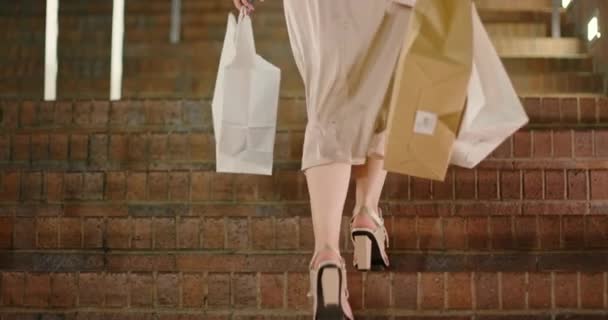 4K ağır çekim alışveriş torbaları. Merdivenlerden çıkan şık topuklu giyen bir kadın. - Video, Çekim