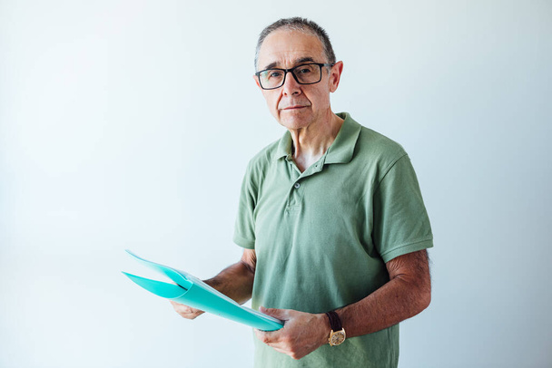 Podnikatel v důchodu muž v zelené polo košile drží složku se zprávou při pohledu do kamery - Fotografie, Obrázek