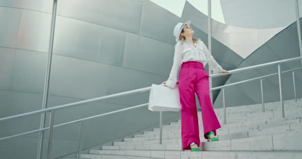 Donna in abito di lusso con fondo rosa, top bianco e borse della spesa è in posa - Filmati, video