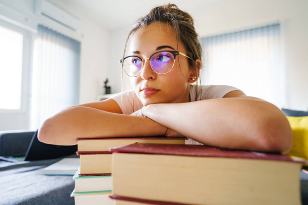 Pohled zepředu portrét mladé studentky bělošky s hlavou opřenou o hromadu knih, která se dívá stranou po studiu a dává si pauzu - koncept vzdělávání - Fotografie, Obrázek