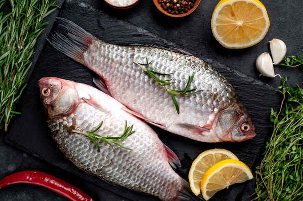 Keresztes ponty hal citrommal és kakukkfűvel egy palatáblán, kőből készült háttérrel. Folyami halak . - Fotó, kép