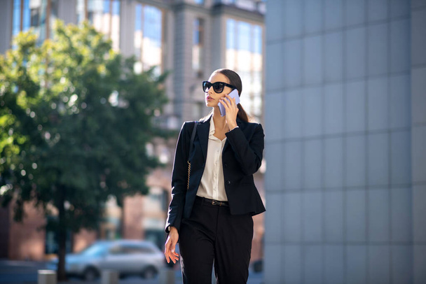 Dark-haired woman in black suit talking on the phone - Fotoğraf, Görsel