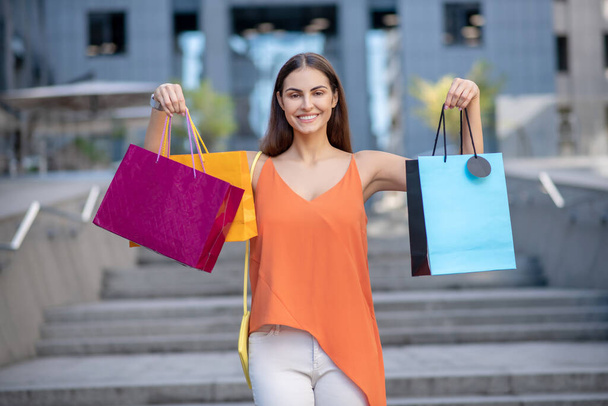 Smiling woman in orange shirt showing shopping bag - Foto, Imagen