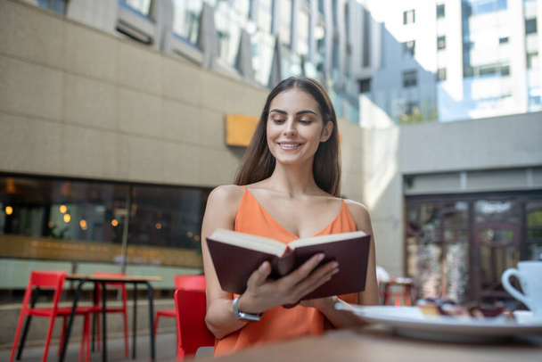 Dark-haired pretty woman holding a book and smiling - Foto, Bild