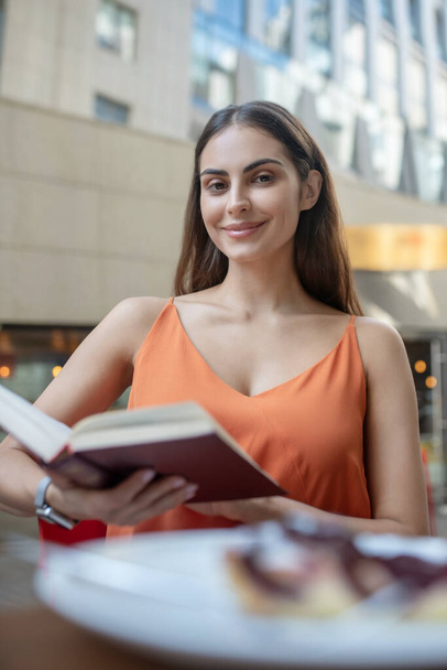 Dark-haired young woman holding a book and smiling - Foto, imagen