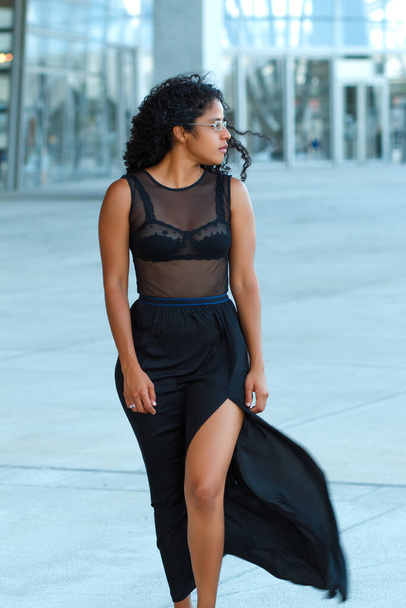 A vertical shot of a curly brunette Hispanic female posing in a beautiful transparent black dress - Foto, Imagem