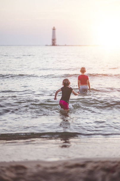 A closeup focus shot of children walking into the sea at sunset - Фото, зображення