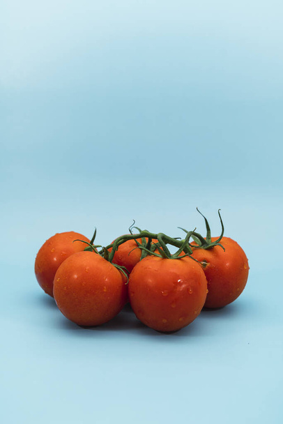 A vertical shot of a bunch of wet red tomatoes on a blue background - Foto, Imagen