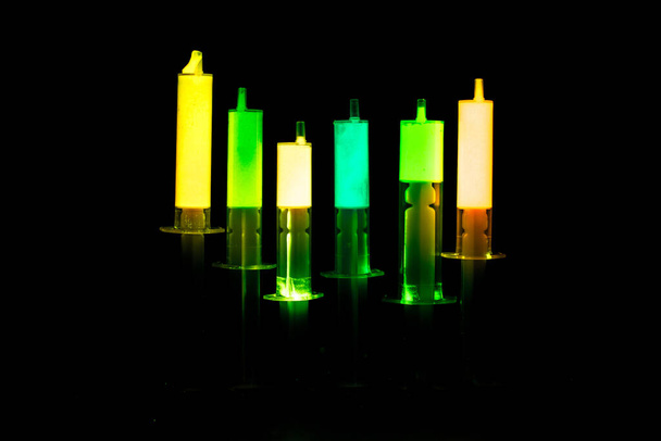 Colored syringes with fluorescent chemicals on the black background - Valokuva, kuva