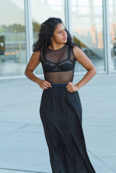 A vertical shot of a curly brunette Hispanic female posing in a beautiful transparent black dress - Foto, Imagem