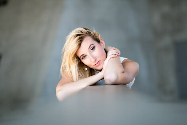 A portrait of an attractive blonde lying female on a grey blurry background - Fotoğraf, Görsel