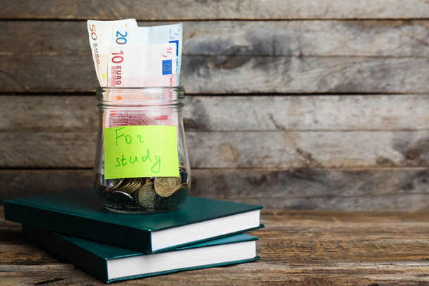Jar with money and books on table. Tuition fees concept - Photo, Image