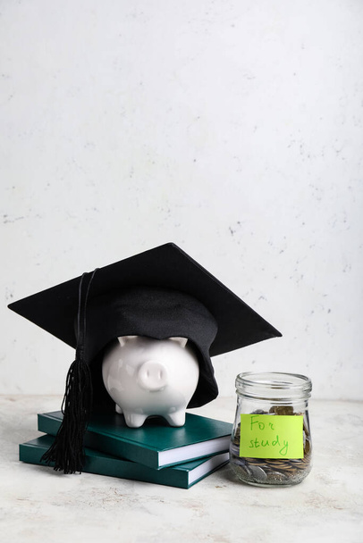 Vaso con monete, salvadanaio, libri e cappello da laurea sul tavolo. Concetto di tasse universitarie - Foto, immagini