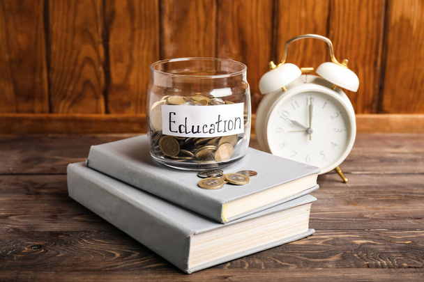 Jar with coins, books and alarm clock on table. Tuition fees concept - Photo, Image