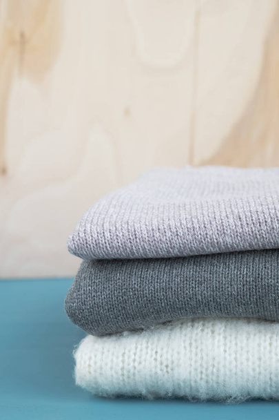 Stack of knitted sweaters on blue wooden table. Warm clothes. Close up, vertical, copy space - Valokuva, kuva