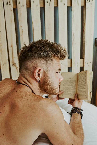 Rear view of a beautiful young man lying in bed reading. Rest concept - Photo, Image