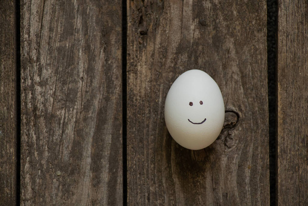 одне біле куряче яйце з розписаною посмішкою на дерев'яному кухонному столі крупним планом
 - Фото, зображення