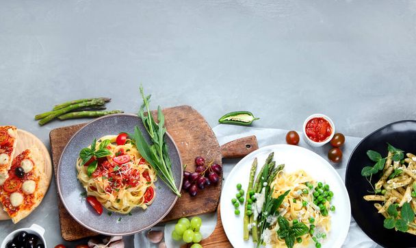 Variety of homemade prepared vegan pasta, pizza and snacks on gray background. Italian cuisine. Top view, flat lay with copyspace - Fotó, kép