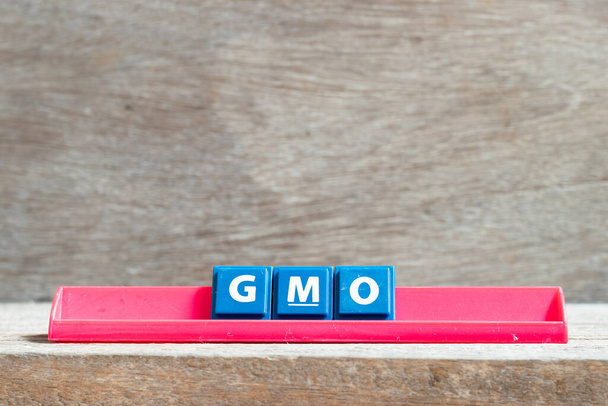 Γράμμα πλακιδίων σε κόκκινη σχάρα με τη λέξη GMO (συντομογραφία των γενετικά τροποποιημένων οργανισμών) σε ξύλινο φόντο - Φωτογραφία, εικόνα