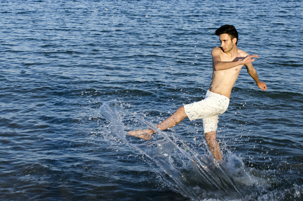 Young man splashing water at the beach, tourist having fun in vacation at the sea - Фото, зображення