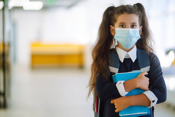 Schoolgirl in a protective mask with a backpack and a textbook in her hands. Security concept, virus protection. Covid-2019. - Foto, Bild
