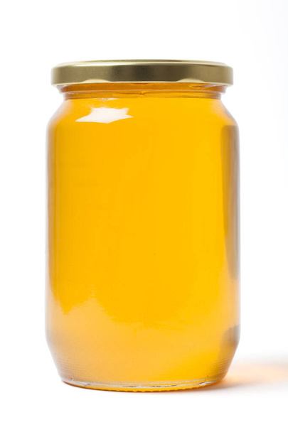 Φρέσκο διαυγές βοτανικό μέλι σε κλειστό καθαρό διάφανο βάζο σε λευκό φόντο. - Φωτογραφία, εικόνα