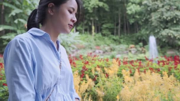 Zpomalený film boční záběr mladé asijské ženy kráčející podél barevné květinové zahrady, pohled na fontánu, šťastný těšit venku, cestování v krásné přírodě, planeta životní prostředí, boj s rakovinou prsu - Záběry, video