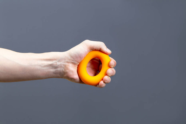 Uomo che tiene un attrezzo da ginnastica in gomma arancione isolato su sfondo grigio, primo piano. Sport e fitness concept - Foto, immagini