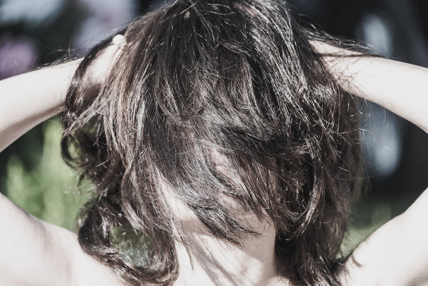 Brunette girl straightens shaggy hair with hands on sunny day - Valokuva, kuva
