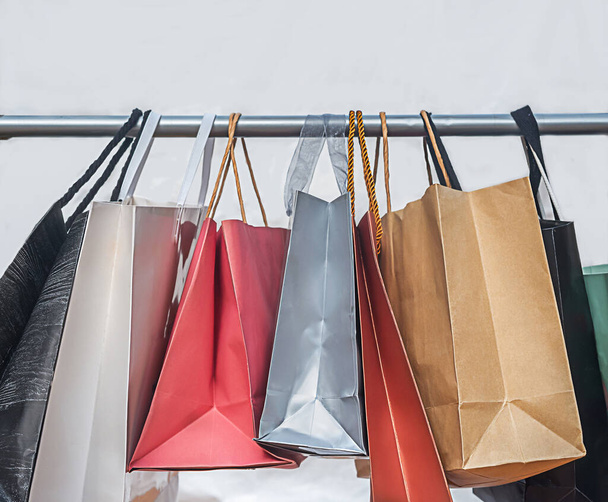 πολύχρωμες τσάντες ψώνια ζυγίζουν σε μια κρεμάστρα σε λευκό φόντο - Φωτογραφία, εικόνα