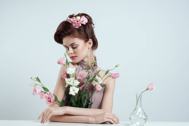 Saçında çiçekler, vazosunda pembe çiçekli arka plan masası olan romantik bir kadın. - Fotoğraf, Görsel