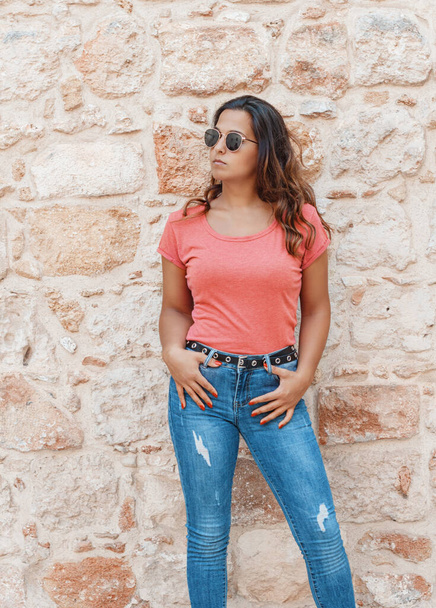 Young women wearing t-shirt and jeans stays near a  wall  - Fotoğraf, Görsel