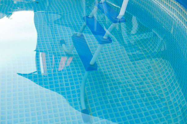 Γαλάζιο νερό και σκάλα για να κατέβει στην πισίνα πλαίσιο. Η αντανάκλαση της οροφής ενός εξοχικού σπιτιού είναι ορατή στο νερό. - Φωτογραφία, εικόνα