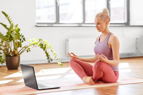 woman with laptop in lotus pose at yoga studio - Foto, afbeelding