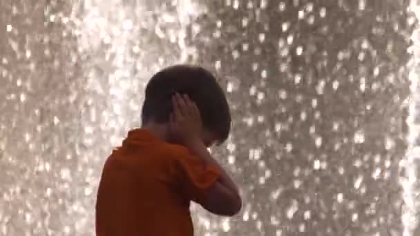 Jongen bedekt zijn oren met handen terwijl hij voor de luidruchtige fontein staat. Gevoelig kind voor lawaai. Kind geïrriteerd en bezorgd over het lawaai van de fontein in het park. Gevoeligheidsstoornis - Video