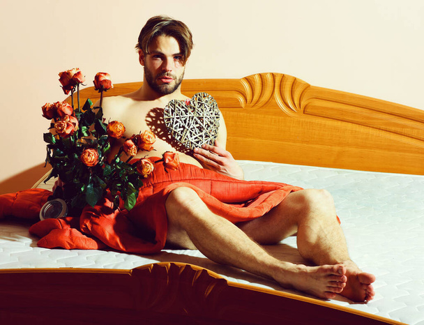 bearded macho man with roses on bed under red blanket holding bouquet - Фото, зображення