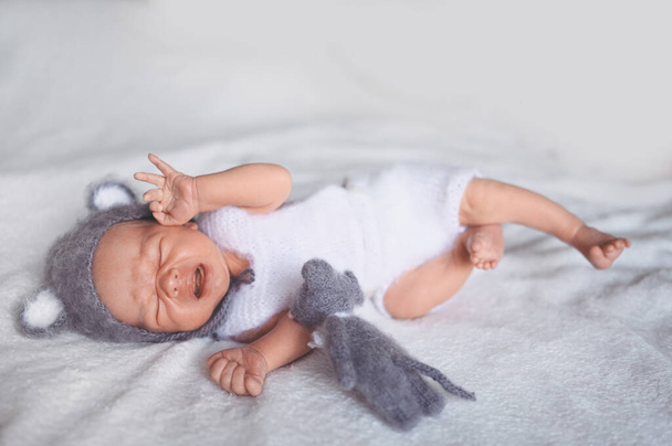 Χαριτωμένο νεογέννητο αγοράκι που κλαίει και κοιμάται σε κούνια με πλεκτό κοστούμι και αυτιά. Πρότυπο συσκευασίας ειδών μωρών. Υγιές παιδί, έννοια του νοσοκομείου και ευτυχισμένη μητρότητα. Βρέφος. Φυτώριο. - Φωτογραφία, εικόνα
