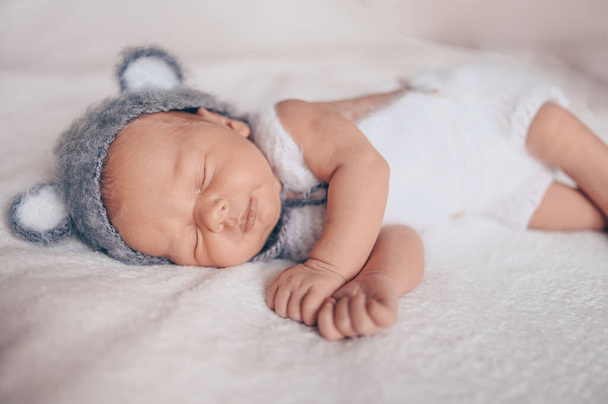 Aranyos, érzelmes, újszülött kisfiú, aki kiságyban alszik, kötött öltönyben, fülekkel. Babaáru csomagolási sablon. Egészséges gyermek, a kórház és a boldog anyaság fogalma. Csecsemő. Gyermekszoba. - Fotó, kép