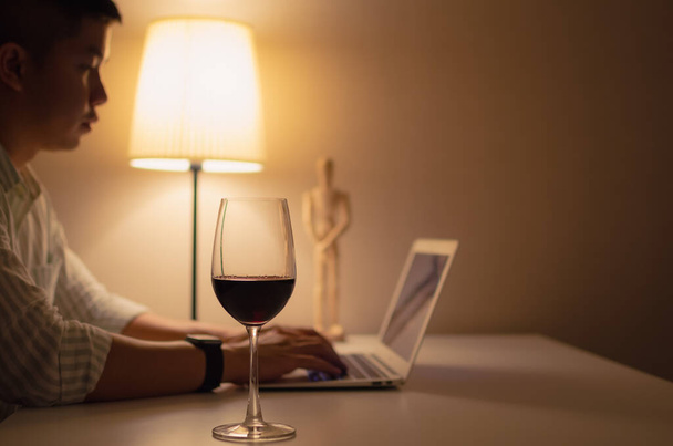 Egy pohár vörösbor teszi az asztalra, hogy igyon és pihenjen, amikor otthon dolgozik.. - Fotó, kép