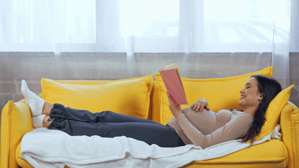 Pregnant woman reading book while lying on couch  - Footage, Video